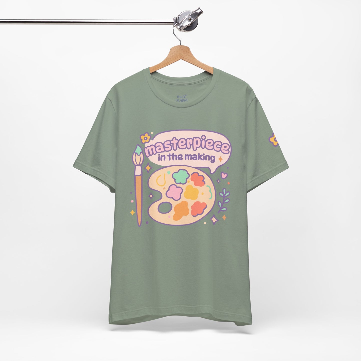 Sage green “Masterpiece in the Making” RubiBloom t-shirt — pastel palette design, cozy aesthetic apparel for creative and gentle personalities.