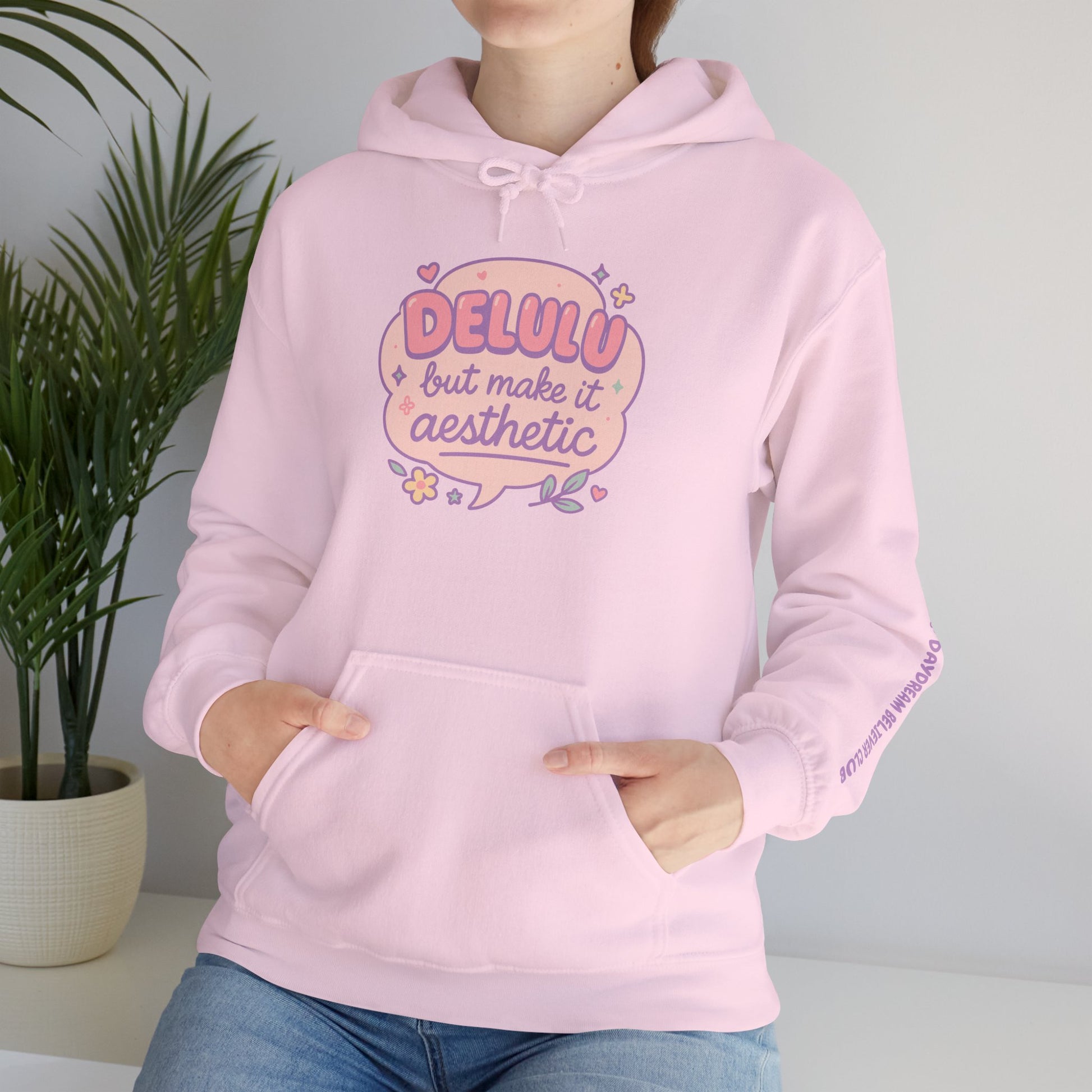 Model wearing pastel pink “Delulu but make it aesthetic” hoodie by RubiBloom — soft cozy sweatshirt with dreamy lettering and delicate sleeve detail, perfect for self-care and chill days.
