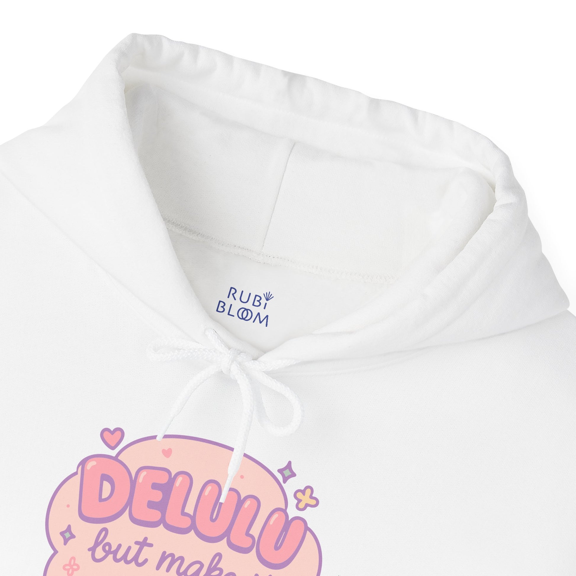 Close-up of pastel print “Delulu but make it aesthetic” on white hoodie — dreamy pink lettering with hearts, sparkles and flowers, RubiBloom cozy aesthetic apparel for soft girls.