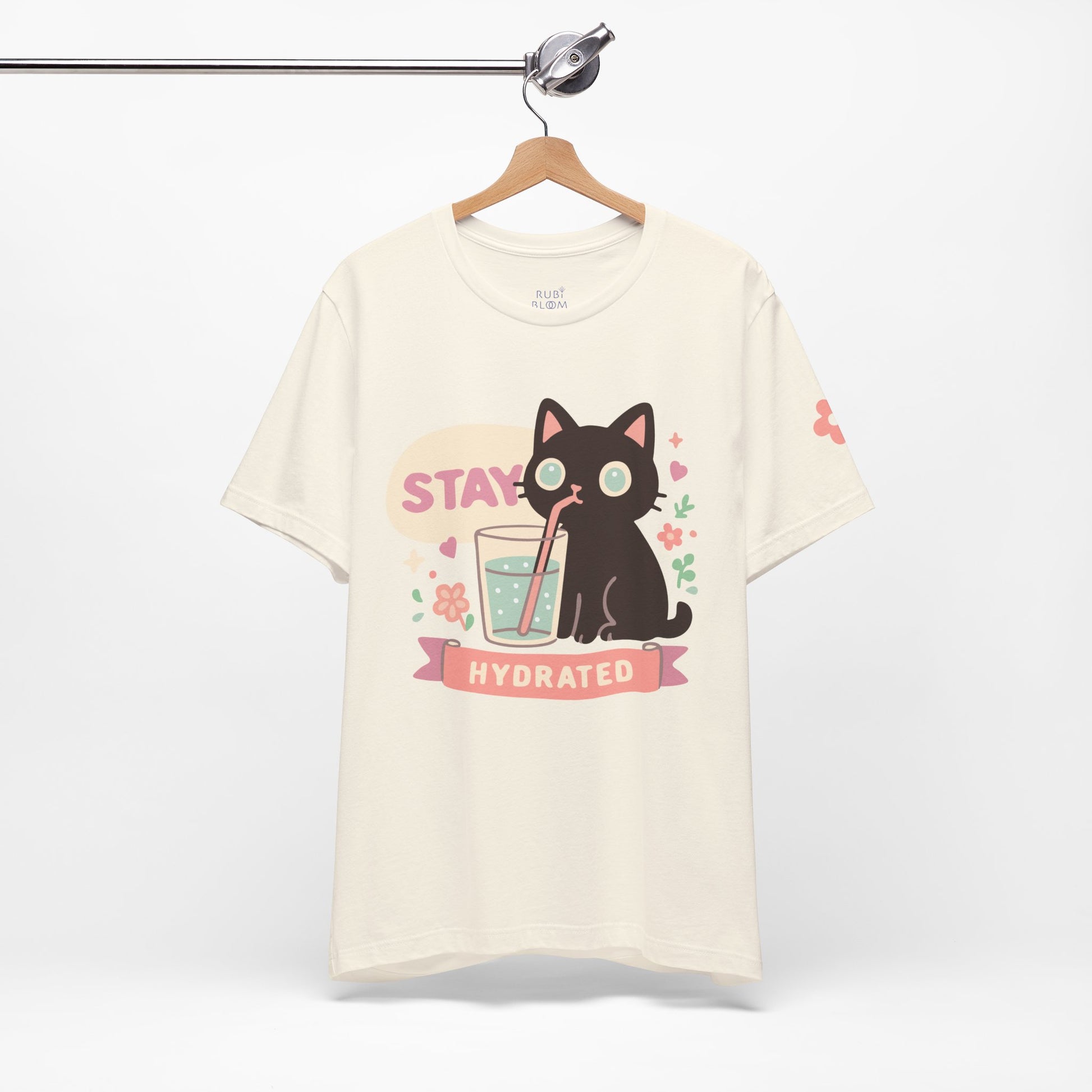 Cream “Stay Hydrated” pastel shirt — kawaii black cat with flowers and glass of water, dreamy aesthetic tee for self-care mornings.