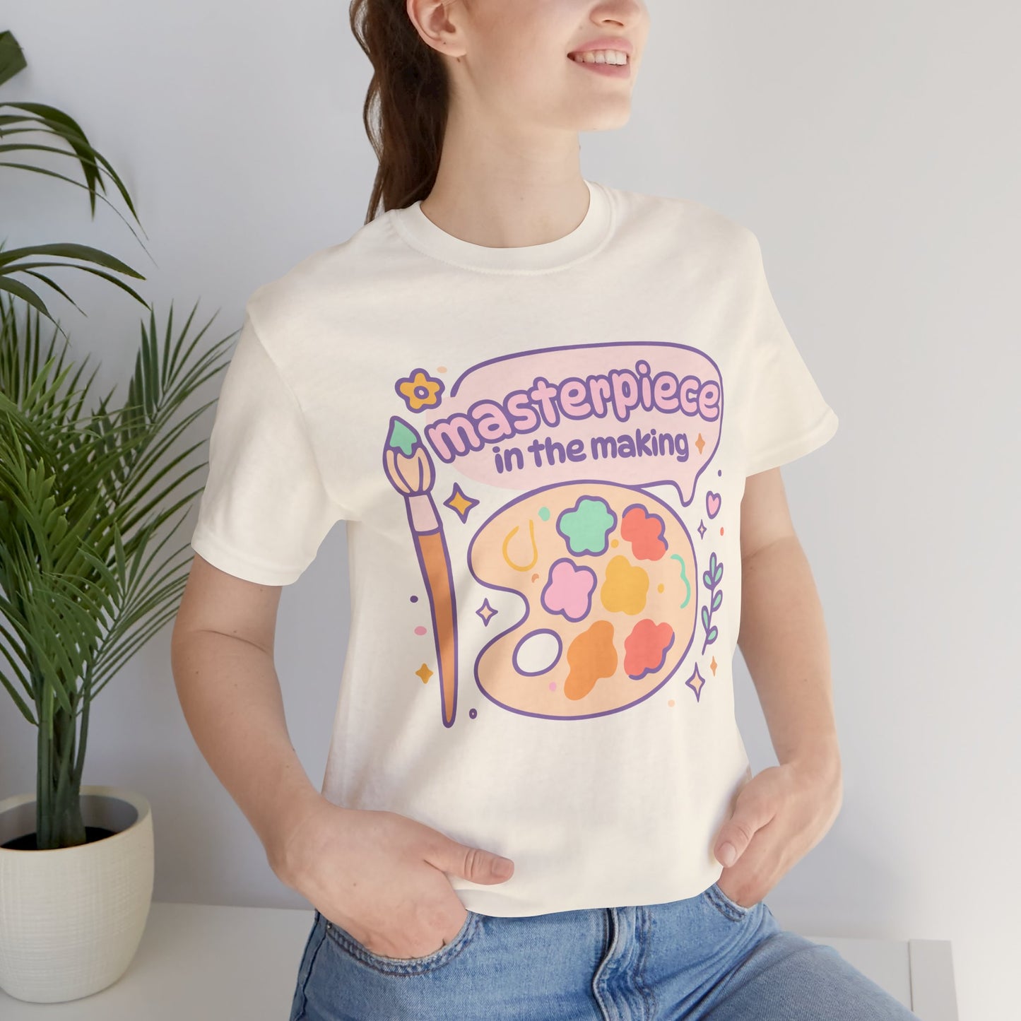 Smiling model wearing pastel “Masterpiece in the Making” shirt — cozy 100% cotton t-shirt with dreamy art print, perfect gift for creative women.